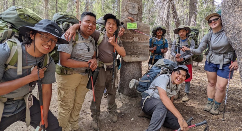 a group of students laugh while posing for a photo on a backpacking course